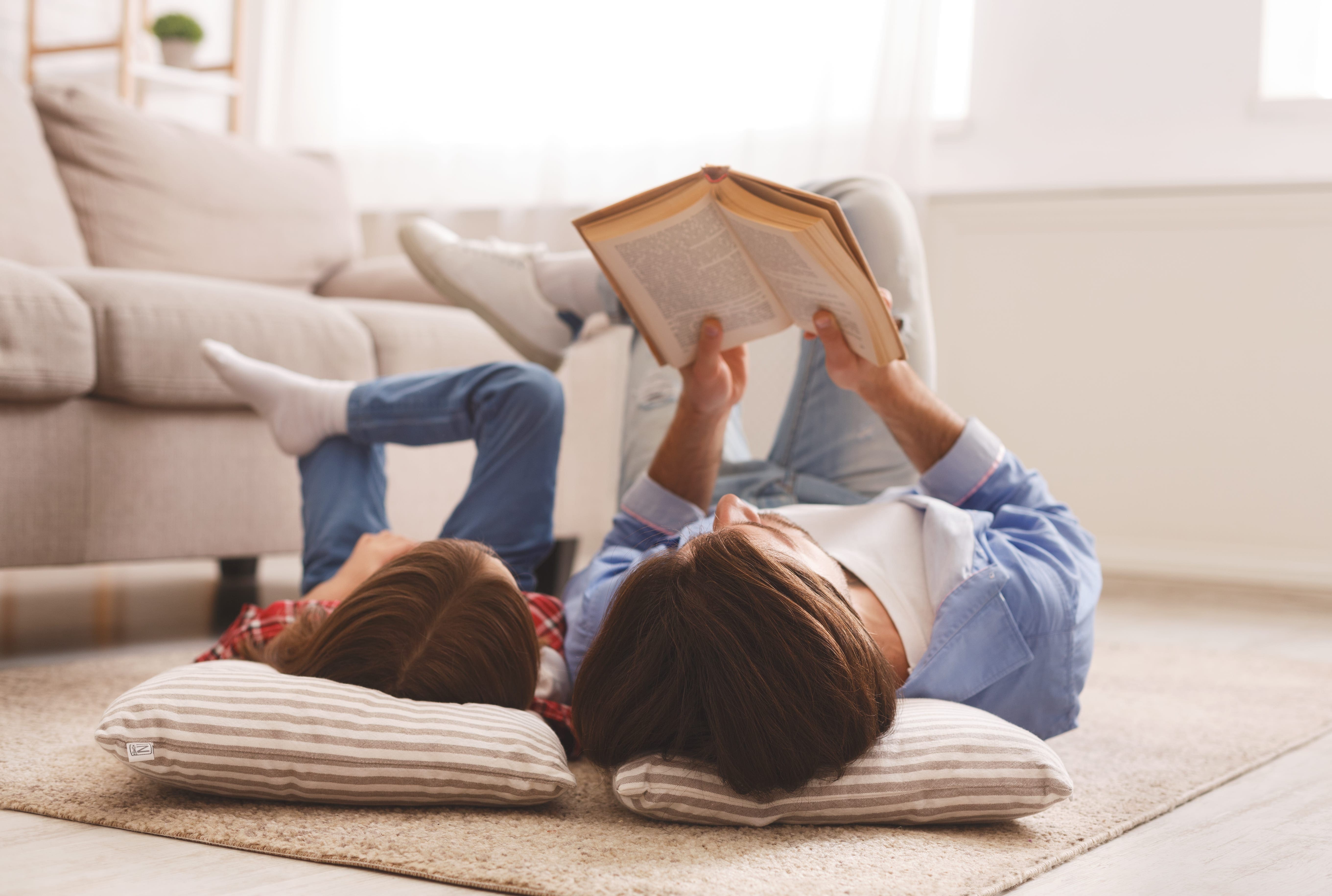 Little girl and father enjoying book together, laying on floor woman and child reading book together