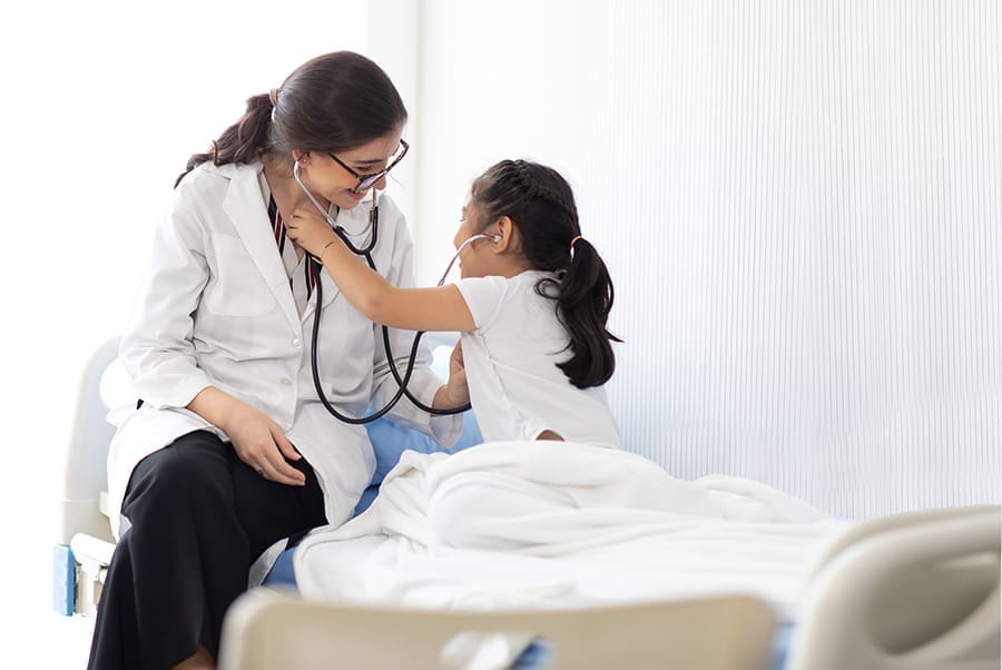Doctor examining a little girl by stethoscope at hospital. Pedia doctor and young patient sitting on hospital bed